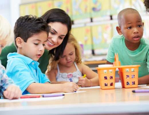 Teacher assisting diverse group of preschool children with drawing activities